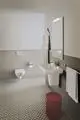 Badezimmeransicht mit Waschtisch, Spiegel und Handtuchhaltern. Ideal Standard Produkte sind sichtbar. Fliesenboden mit geometrischem Muster, Handtuch und Bademantel hängen an der Wand.